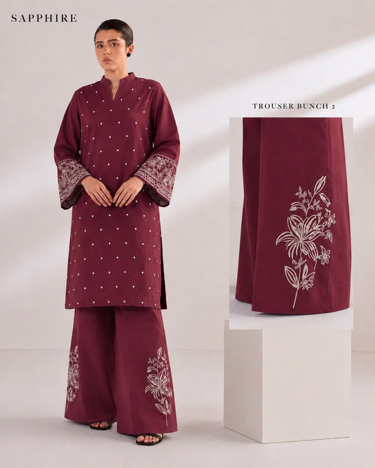A model wears a deep maroon three-piece kurta set with off-white embroidery and silver mirror work, shown alongside a close-up inset of the trouser fabric with floral embroidery.