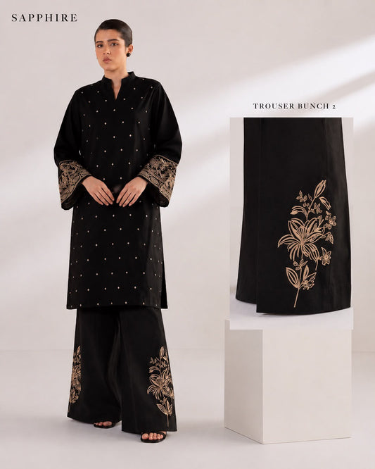 A model wears a black traditional tunic and wide-leg trouser set with gold embroidery and motiffs, shown against a light studio background. A side panel inset highlights the trouser embroidery, and the brand name SAPPHIRE appears in the top left.